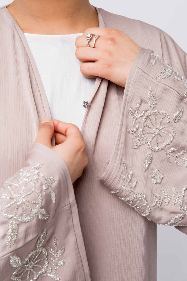   Nude abaya with flowy silhouette and embellished sleeves, perfect for Ramadan fashion. 