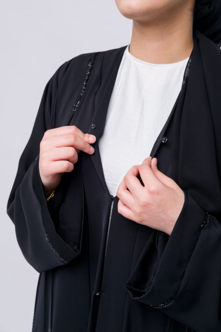 Modest black abaya with long sleeves and light embellishments, perfect for hijabi style lovers.