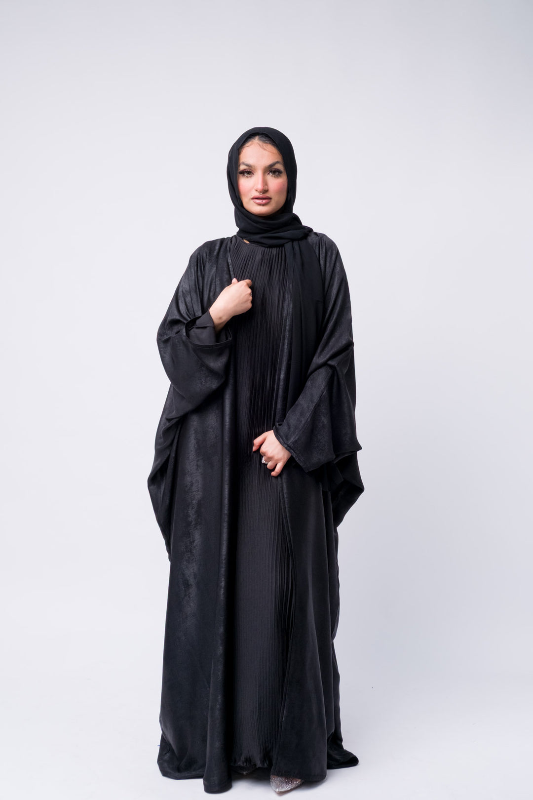 Black satin pleated abaya with loose fit and batwing sleeves, perfect for modest yet chic styling.
