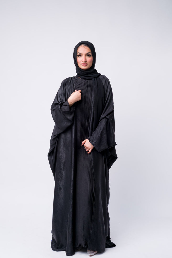 Black satin pleated abaya with loose fit and batwing sleeves, perfect for modest yet chic styling.