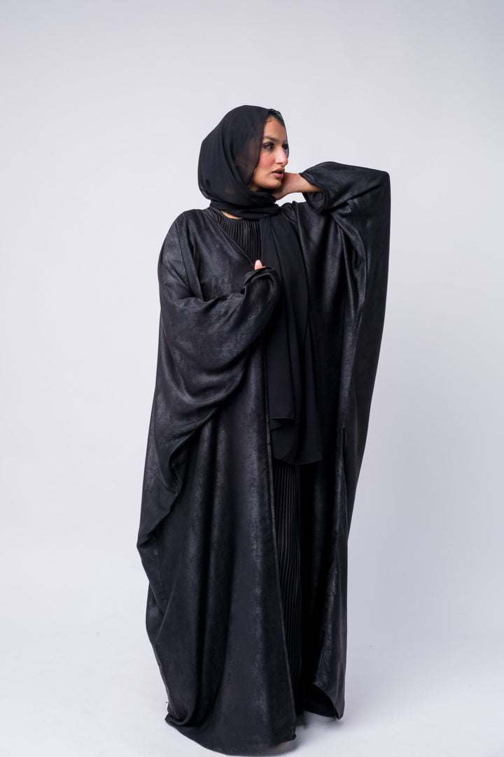 Flowy black abaya dress with long sleeves and layered pleats, suitable for hijabi fashion and gatherings.